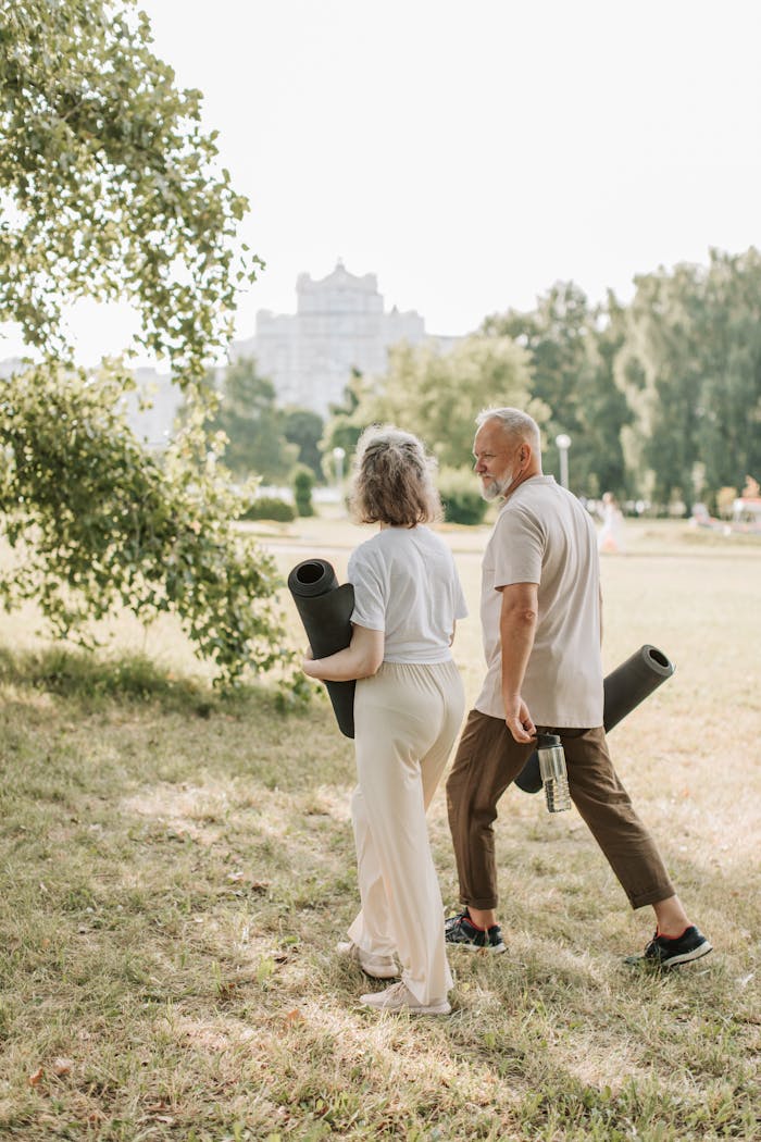 services-03 Elderly couple walking in park carrying yoga mats for a wellness session.