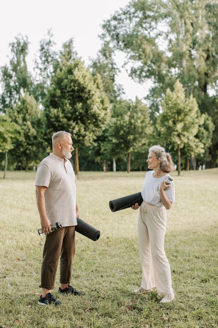 services-02 Senior couple holding yoga mats, enjoying a sunny day outdoors in a green park.