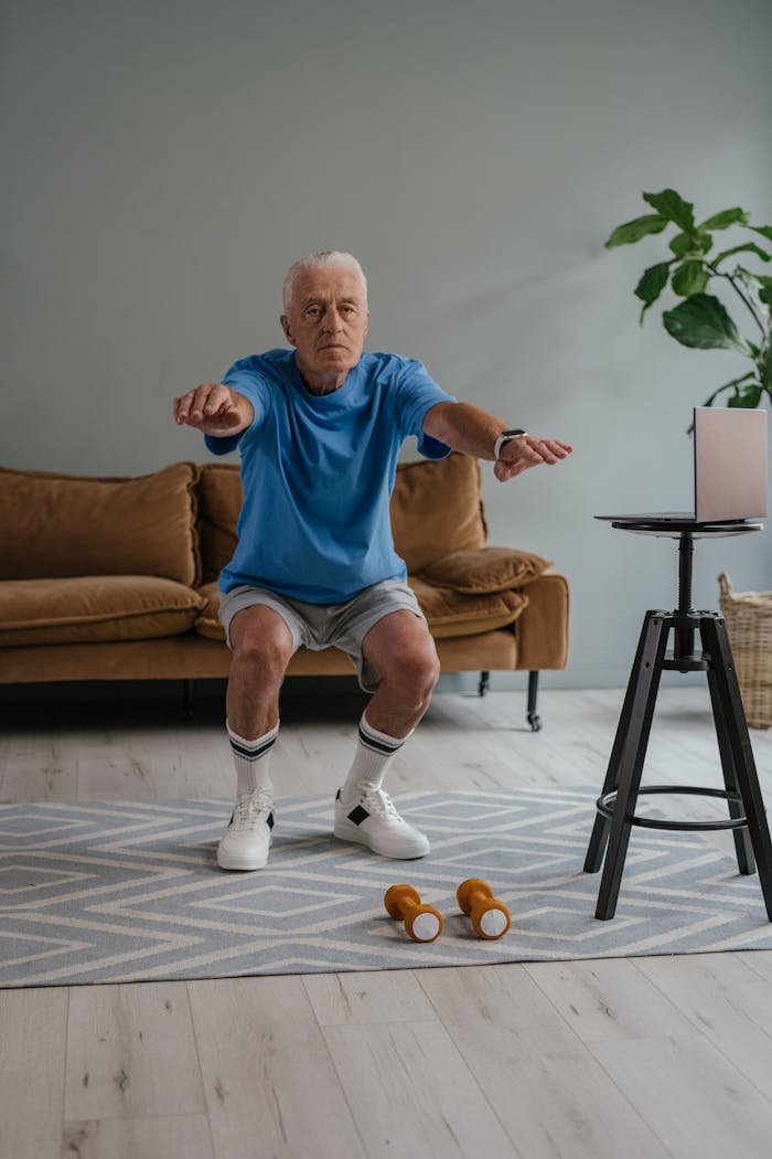 gallery-6 A senior man performing squats with dumbbells on a mat indoors for a healthy lifestyle.